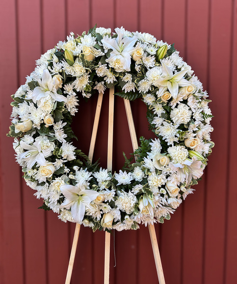 Standing wreath of all-white flowers on an easel for a funeral.