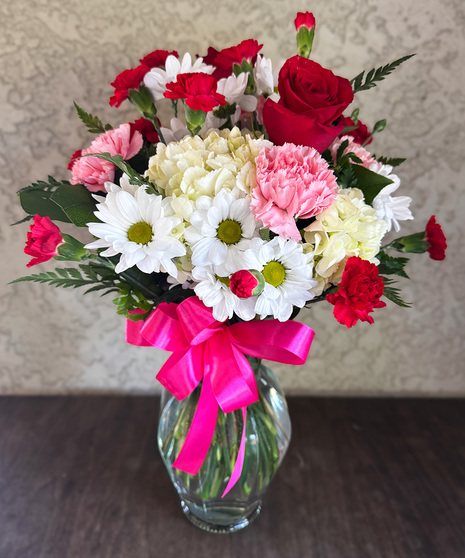 Heartstring Medley floral arrangement with red roses, white hydrangea, pink carnations, and red mini-carnations in a glass vase with a satin bow
