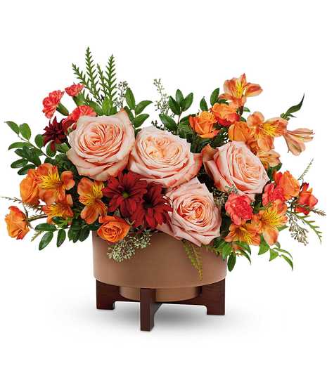 Copper Celebration Bouquet with peach roses, orange spray roses, mini-carnations, alstroemeria, and bronze daisies in a copper planter with stand